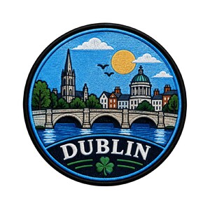 Puede incluir: Un parche bordado circular que muestra un cielo azul con un sol amarillo, nubes blancas y dos pájaros. La escena representa un puente de piedra sobre el agua, edificios urbanos y una torre de iglesia. La palabra DUBLIN aparece en blanco sobre un trébol verde.