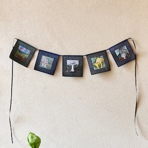 May include: A black and white banner with images of mushrooms hangs on a beige wall. A peace lily plant with green leaves and a white flower is in the foreground.