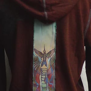 May include: A maroon hoodie with a colorful hummingbird design on the back. The design features a hummingbird in flight with a blue, green, and purple background.