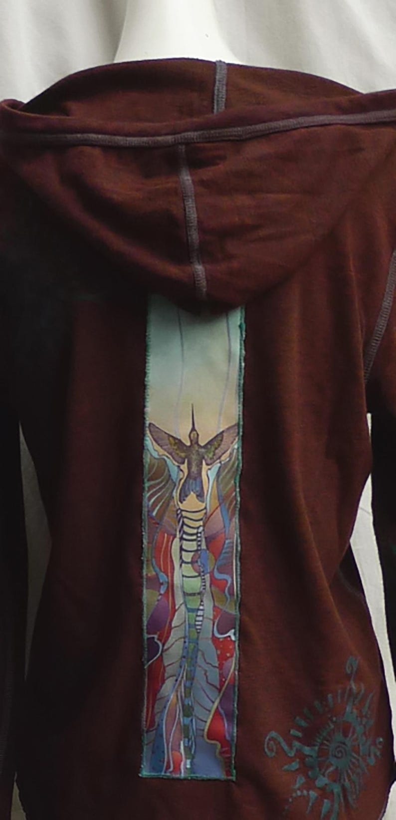 May include: A maroon hoodie with a colorful hummingbird design on the back. The design features a hummingbird in flight with a blue, green, and purple background.