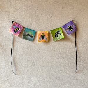 May include: A colorful banner with five fabric flags featuring illustrations of bumblebees. Each flag is a different color, with the bees depicted in realistic detail.