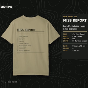 May include: A tan short-sleeved t-shirt featuring a black graphic on the back that resembles a form titled MISS REPORT. The design includes a checklist with options like SHOOTER ERROR, WIND CALL, and a checked box for IT WAS THE WIND.