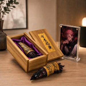 May include: A wooden box with a purple satin lining containing a dark, textured, finger-like object wrapped in a tan paper scroll with black Japanese characters. A matching object lies in front, and a clear acrylic frame displays a character illustration.