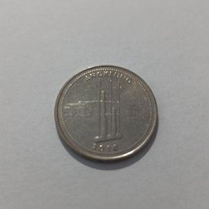 May include: A silver-colored circular coin featuring an embossed image of an angklung musical instrument in the center. The word ANKLUNG is printed in an arc above the instrument, and the year 2010 is inscribed at the bottom of the coin face.
