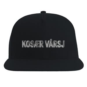 Op de afbeelding: Een zwarte baseballpet met een platte klep en een gestructureerde kroon. Op de voorkant van de pet staat de tekst KOSÆR VÅRSJ geborduurd in lichtgrijs, getextureerd garen, dat duidelijk afsteekt tegen de zwarte stof van de pet.