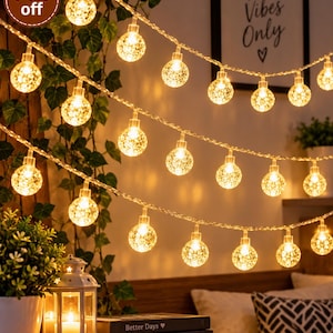 Op de afbeelding: Een lichtsnoer met warmwitte led-bollen met een getextureerd, bubbelachtig oppervlak. De lampjes zijn in meerdere strengen gerangschikt en stralen een zachte gloed uit. Een cirkelvormige badge toont de tekst 74% off in witte letters.
