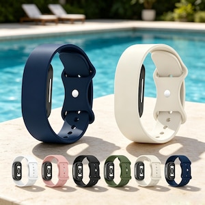 May include: Two fitness tracker bands in navy blue and cream are displayed upright, featuring a smooth silicone finish and a central metal stud closure. Below, a row of six additional bands in white, pink, black, olive green, cream, and navy blue.