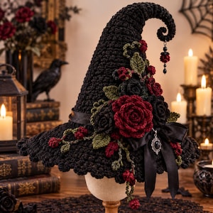 May include: A black crocheted pointed hat featuring a curled tip with a dangling bead charm. The hat is adorned with dark red and black crocheted roses, green leaves, and small red berries. A black satin ribbon is tied in a bow with a silver pendant.