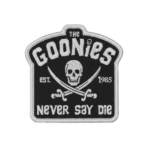 Puede incluir: Un parche bordado en blanco y negro con un diseño de calavera y tibias cruzadas. El texto dice THE GOONIES, est. 1985 y NEVER SAY DIE. El parche tiene un borde blanco y un fondo negro con detalles en hilo blanco del diseño pirata.