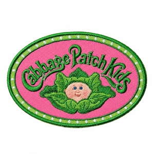 May include: An oval-shaped embroidered patch featuring a bright pink background with a green border accented by white dots. The text Cabbage Patch Kids is stitched in green above a central graphic of a baby face nestled inside green cabbage leaves.