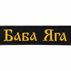 Op de afbeelding: Een rechthoekige geborduurde patch met een zwarte achtergrond en een gouden rand. De tekst "Баба Яга" is in goudkleurig draad in het midden van de patch geborduurd in een gestileerd Cyrillisch lettertype. De patch heeft een nette afwerking.