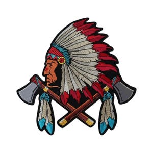 May include: An embroidered patch featuring a profile of a person wearing a large feathered headdress in red, white, and blue. Two crossed tomahawks with brown handles and grey blades are positioned behind the head, each adorned with hanging feathers.