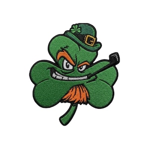 Puede incluir: Un parche bordado que presenta un personaje de trébol verde con una expresión traviesa, que lleva un sombrero de duende verde con una hebilla dorada. El personaje tiene cejas y barba naranjas, y sostiene un palo de golf negro en la boca.