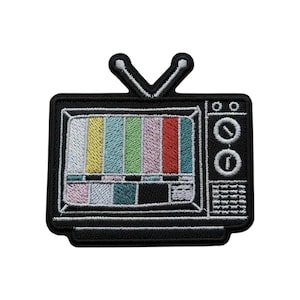 Puede incluir: Un parche bordado con forma de televisor antiguo con dos antenas. La pantalla muestra un patrón de prueba vertical de colores en amarillo, azul, verde, rosa y rojo, con una sección de cuadrícula en blanco y negro en la parte inferior y perillas.