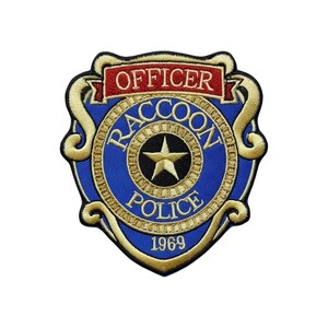 May include: An embroidered patch shaped like a shield with a blue centre and gold border. It features the text OFFICER at the top in red, RACCOON POLICE in gold, and 1969 at the bottom. A gold star is centred within a circular gold frame.