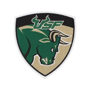 May include: A shield-shaped embroidered patch featuring a green bull head in profile with tan and black accents. The text USF is embroidered in green above the bull. The patch has a black background and a white border around the entire edge.