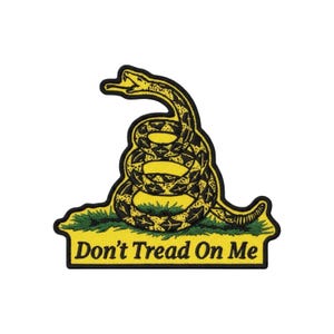 May include: A yellow and black embroidered patch featuring a coiled rattlesnake on a patch of green grass. The design includes the text Don't Tread On Me in black lettering at the bottom, with a black border outlining the entire shape of the patch.