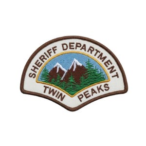 Puede incluir: Un parche bordado semicircular con un borde marrón. El centro presenta un cielo azul claro, montañas marrones con picos nevados blancos y pinos verdes. El texto dice SHERIFF DEPARTMENT TWIN PEAKS en letras de color marrón.