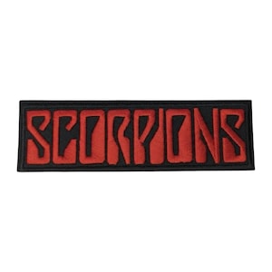 May include: A rectangular embroidered patch featuring the word SCORPIONS in bold, red, stylised capital letters. The text is set against a solid black background with a thick black border, creating a high-contrast design for this fabric accessory.