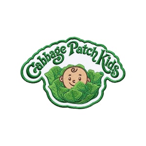 May include: An embroidered patch featuring the text Cabbage Patch Kids in green cursive lettering above a graphic of a tan-skinned baby face peeking out from a cluster of textured green cabbage leaves, all outlined with a thick green border.