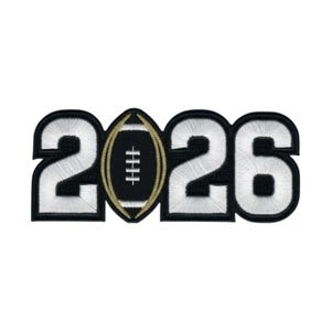 May include: An embroidered patch featuring the number 2026, where the zero is replaced by a black and gold American football graphic. The numbers are white with thick black borders, and the football has white laces and gold stitching details.