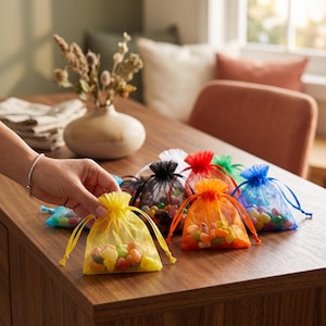 May include: A collection of small, semi-transparent organza drawstring bags in various colors including yellow, orange, red, blue, green, black, and white, each filled with assorted colorful jelly bean candies.