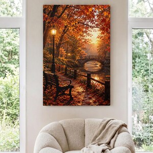 May include: A vertical rectangular wall art print depicting an autumn park scene with a black metal bench, a glowing street lamp, and a stone bridge over a calm body of water. The landscape is filled with vibrant orange and yellow foliage.
