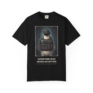 Könnte beinhalten: Ein schwarzes T-Shirt mit kurzen Ärmeln und einem Aufdruck eines Pinguins, der eine taktische Weste und ein Headset vor Server-Racks trägt. Unter dem Bild steht der Text: DOWNTIME WAS NEVER AN OPTION. The servers will stay on. The penguin has decided.