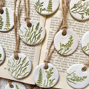 May include: A set of 10 white ceramic ornaments with green floral designs. Each ornament has a hole at the top for hanging. The ornaments are strung together with twine.