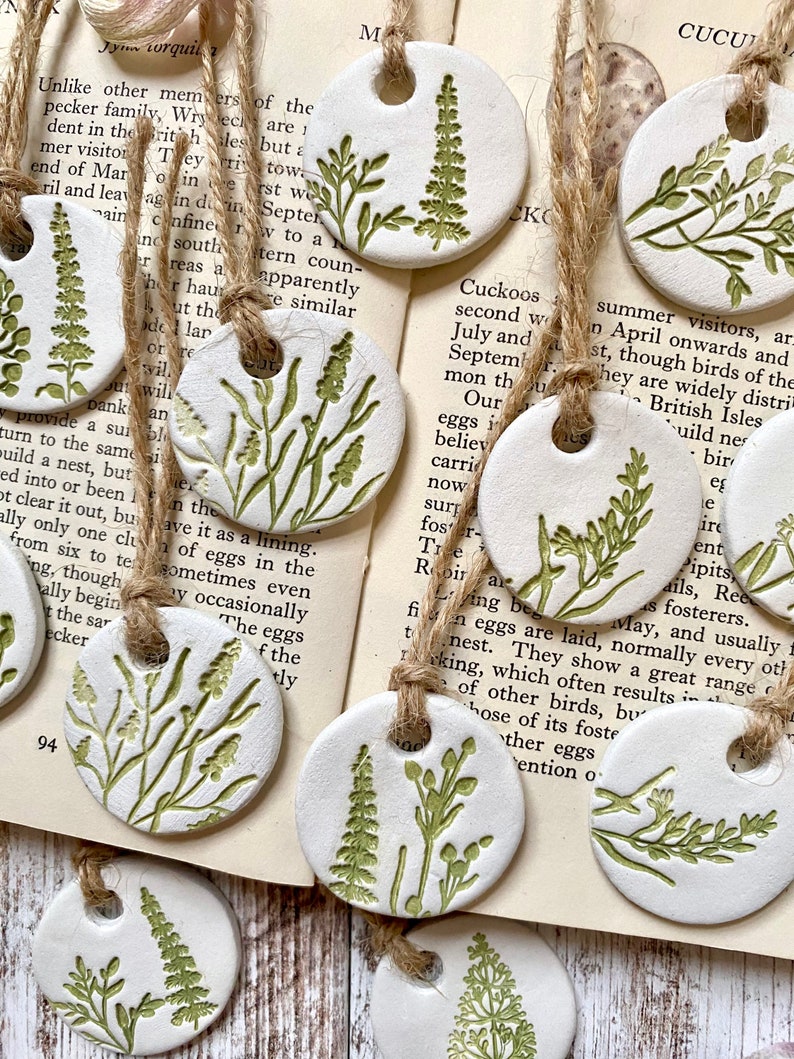May include: A set of 10 white ceramic ornaments with green floral designs. Each ornament has a hole at the top for hanging. The ornaments are strung together with twine.
