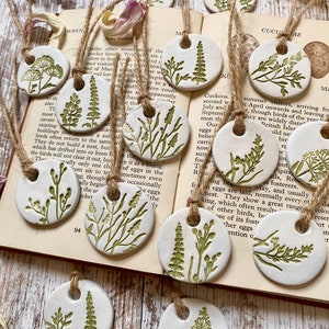 May include: A set of ten white ceramic ornaments with green floral designs. Each ornament has a hole for hanging and is strung with twine.