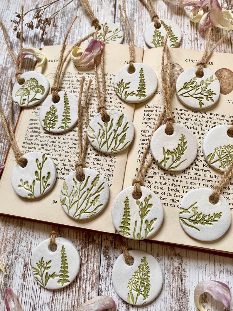 May include: A set of ten white ceramic ornaments with green floral designs. Each ornament has a hole for hanging and is strung with twine.