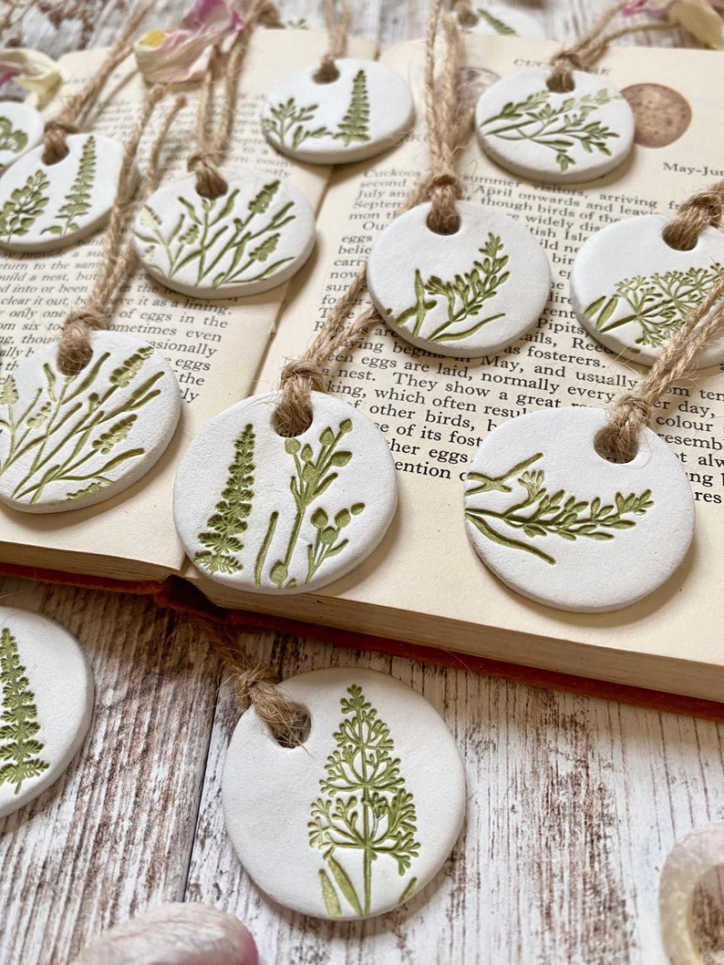 May include: A set of 10 white ceramic ornaments with green floral designs. Each ornament has a hole at the top for hanging. The ornaments are arranged on a book with text about birds.