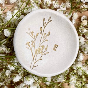 May include: White ceramic trinket dish with a gold floral design and the letter "E" in gold.