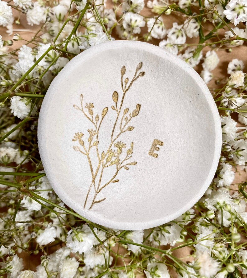 May include: White ceramic trinket dish with a gold floral design and the letter "E" in gold.