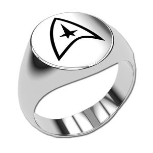 Könnte beinhalten: Silberner Ring mit weißer Oberfläche, die ein schwarzes Pfeil- und Sterndesign zeigt. Der Ring hat eine glatte, polierte Oberfläche und einen abgerundeten Ring. Das Design ist ein stilisiertes Emblem.