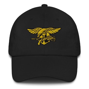 Könnte beinhalten: Eine schwarze Baseballkappe mit einem goldenen gestickten Navy SEAL-Abzeichen. Das Abzeichen zeigt einen geflügelten Adler, einen Dreizack und ein Gewehr.