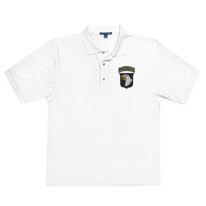 May include: White polo shirt with a black and white embroidered patch featuring an eagle and the word "AIRBORNE" in yellow.