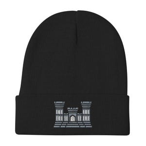 May include: Black knit beanie with a folded brim. The front of the beanie features a light gray embroidered emblem of a castle with three towers. The beanie is made of a soft, warm material, suitable for cold weather.
