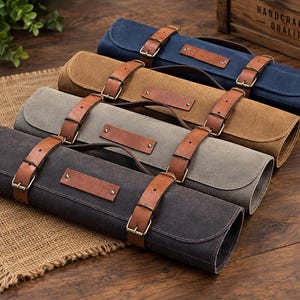 Puede incluir: Cuatro estuches cilíndricos de lona para herramientas en gris oscuro, gris claro, beige y azul marino. Cada estuche cuenta con dos correas de cuero marrón con hebillas metálicas, un asa de cuero y un parche rectangular de cuero con remaches.