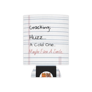 May include: A white can cooler featuring a lined notebook paper pattern with the black text Cracking: Huzz.... A Cold One... and the red text Maybe Even A Smile.... At the bottom, a small black rectangular patch displays an orange cat and a brown dog.