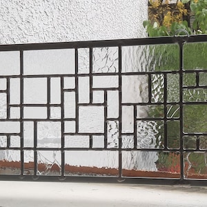 May include: Rectangular stained glass window with a geometric pattern. The window features clear and textured glass panes set within a dark metal frame. The design is composed of various rectangular and square shapes.