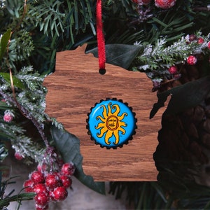 Puede incluir: Un adorno de madera con forma del estado de Wisconsin con un diseño de sol azul y amarillo en el centro.