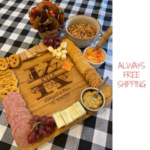 May include: Personalized wooden serving board with the names Kyle and Abigail & Pere, established 10.06.2019, engraved on the surface. The board is filled with various snacks, including crackers, cheese, salami, grapes, and dips.