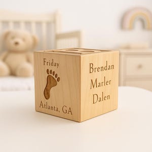May include: A light-coloured wooden block with engraved text and a footprint design. The block features the word "Friday", a footprint, the names "Brendan, Marler, Dalen", and "Atlanta, GA". The block is a decorative item.