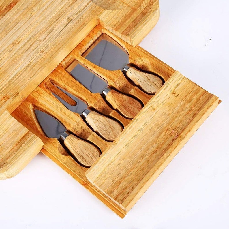 May include: A wooden cheese board with a built-in drawer that holds five cheese knives with wooden handles.