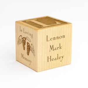 Puede incluir: Un bloque de madera con la letra "L" grabada en la parte superior. El bloque presenta las palabras "In Loving Memory" con alas de ángel y huellas, y los nombres "Lennon Mark Healey" también están grabados.