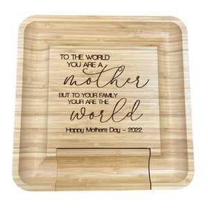 May include: A wooden serving tray with a raised edge and a cutout in the center. The tray is engraved with the text "To the world you are a mother but to your family your are the world Happy Mother's Day ~ 2022".