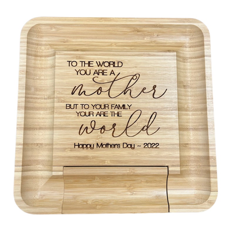 May include: A wooden serving tray with a raised edge and a cutout in the center. The tray is engraved with the text "To the world you are a mother but to your family your are the world Happy Mother's Day ~ 2022".