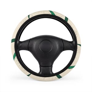 May include: A black steering wheel fitted with a circular cover featuring a cream-colored background and a repeating pattern of dark green curved leaf-like shapes. The cover has black trim along the inner and outer edges of the steering wheel.